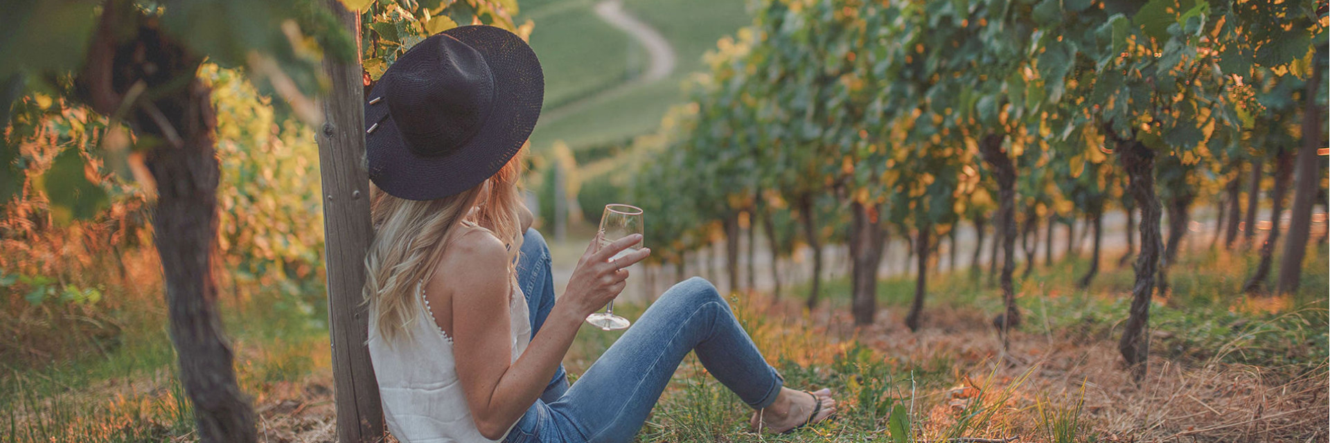 Photo of a woman enjoying a glass of white wine at sunset over the vines.