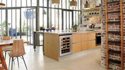 Petite taille d'armoire à vin porte vitrée avec cadre inox dans une cuisine ouverte avec baie vitrée au design industriel, mur de briques et meubles en bois clair. Petite taille d'armoire à vin porte vitrée avec cadre inox dans une cuisine ouverte avec baie vitrée au design industriel, mur de briques et meubles en bois clair.