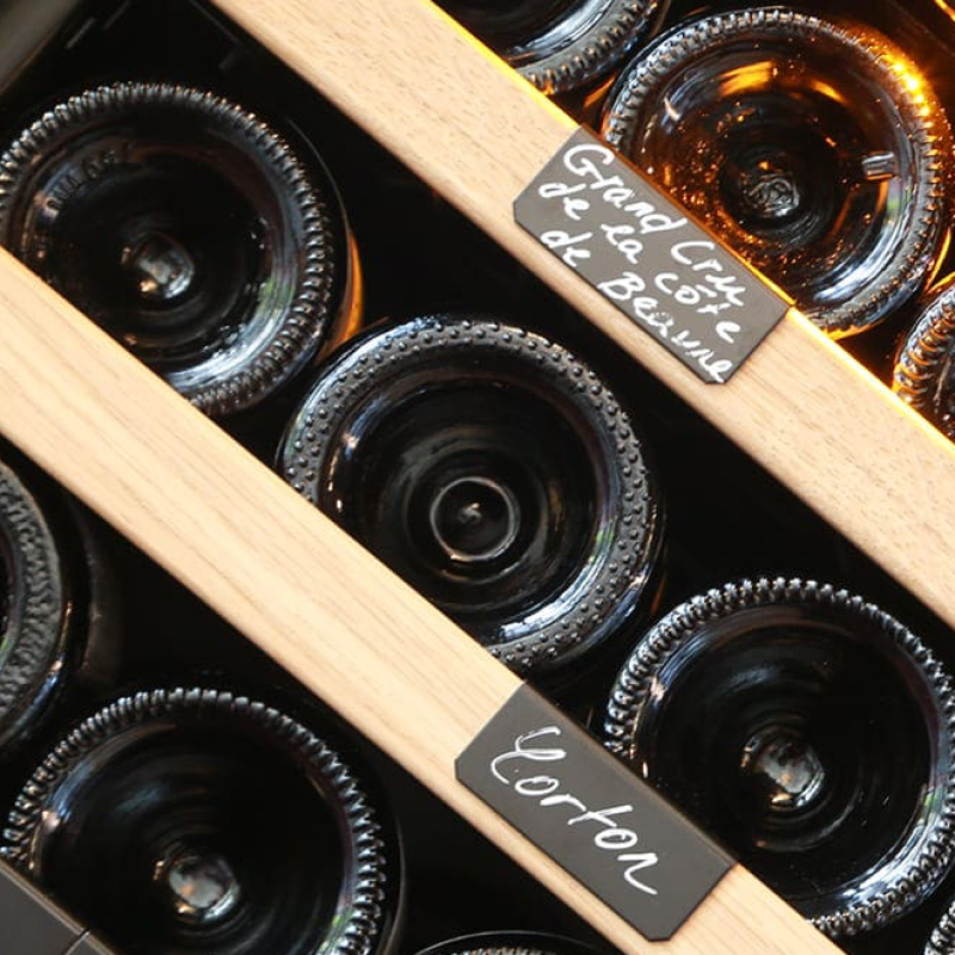 Lagerung im Weinkeller – Metallregale mit einzelnen Flaschenhaltern, Front aus naturfarbenem Eichenholz.